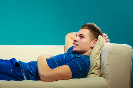 Young man relaxing on couch, teen happy boy laying lazy on bed blue background