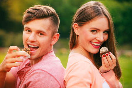Love and dating concept. Young fashionable smiling couple lovers with candy sweets muffins on picnic outdoor.の写真素材