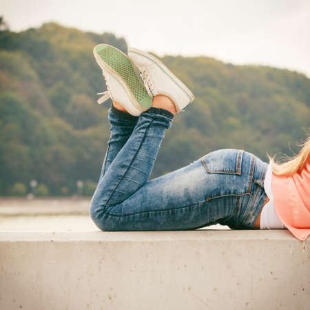 Female fashion concept. Part body of stylish woman lying outside wearing jeans and sneakers.の写真素材