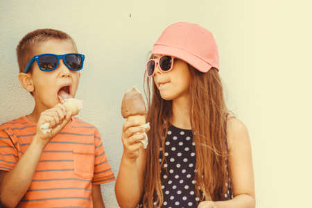 Kids eating gelato and soft serve ice cream. Boy and little girl in sunglasses enjoying summer holidays vacation.  の写真素材
