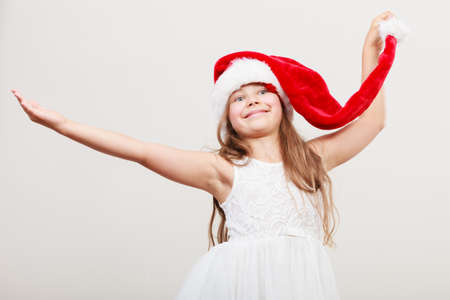 Happy cute little girl kid in red santa claus hat and white dress. Chrtistmas holiday season.の写真素材