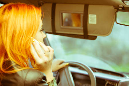 Concept of danger driving. Young woman driver redhaired girl talking on mobile phone smartphone...