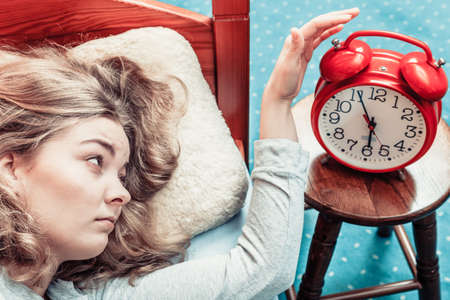 Woman waking up in bed turning off alarm clock. Young girl in the morning.