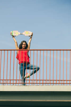 Cool skate young long haired girl holding skateboard on the urban bridge. Active lifestyle funky...