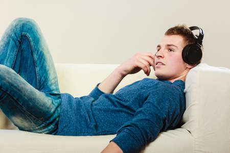 leisure and lifestyle concept. Young handsome man with headphones lying on couch listening music at homeの写真素材