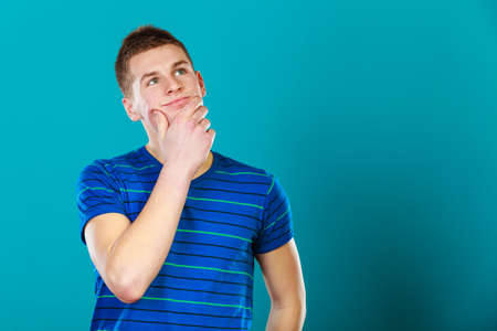 Young man thinking, thoughtful face expression on blue