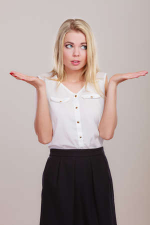 Shrugging woman in doubt doing shrug, attractive confused girl gesturing do not know sign on gray backgroundの写真素材