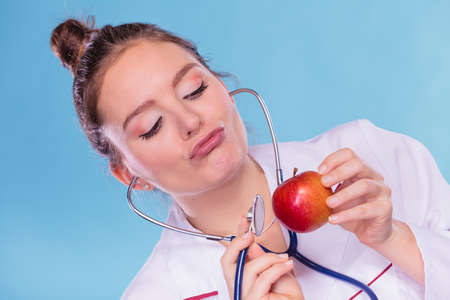Disgusted dietitian nutritionist checking examine apple fruit with stethoscope. Woman with food....