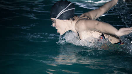 Woman athlete swimming performing butterfly style stroke in pool. Active human swimmer taking...