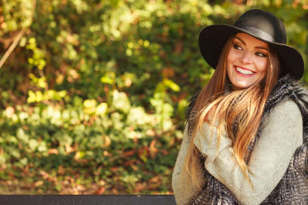 Gorgeous stylish young woman wearing fashionable clothes. Portrait of girl in black hat sitting on bench in park.の写真素材