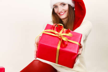 Christmas winter happiness concept. Smiling latin woman wearing santa helper hat holding present red...