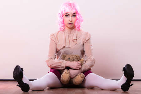 Mental disorder concept. Young childlike woman wearing like puppet doll holding teddy bear toy studio shotの写真素材