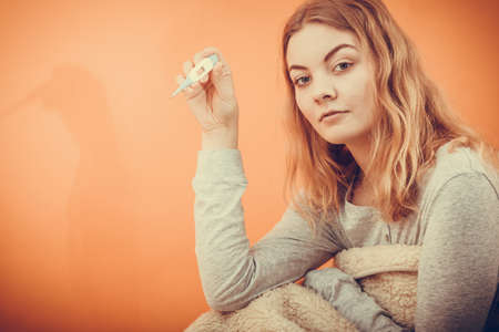 Sick ill woman under blanket with digital thermometer. Young girl having high fever measuring temperature. Health.の写真素材