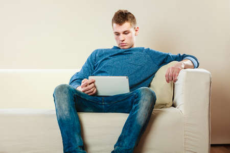 Modern technology leisure and relaxation concept. Young man with pc computer digital tablet on couchの写真素材