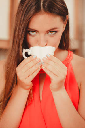 Pretty woman drinking tea or coffee at home. Gorgeous young girl with hot beverage relaxing in kitchen.の写真素材