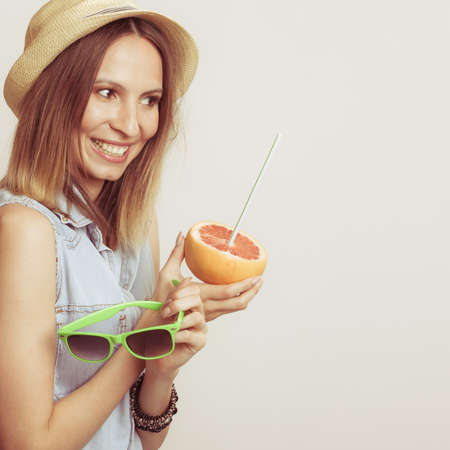 Happy glad woman tourist in straw hat holding sunglasses and grapefruit citrus fruit. Healthy diet food. Summer vacation holidays concept.の写真素材