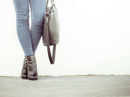 Autumn fashion outfit. Fashionable woman long legs in denim pants black stylish high heels shoes and handbag outdoor on city streetの写真素材