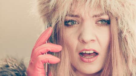 Portrait of scared afraid pretty woman talking on mobile phone. Gorgeous young girl in fur winter...