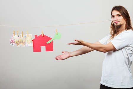 Concept of real estate and deal. Seller man with house model and banknotes. Selling and buying proposition.の写真素材