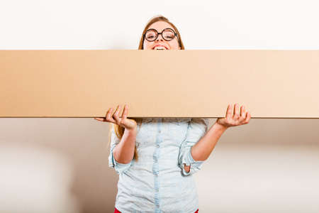 Happy woman moving into new apartment house carrying carton box with furniture. Young girl holding blank empty copyspace banner.の写真素材