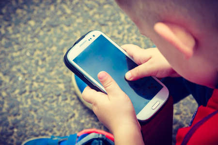Little boy child kid playing games on smartphone mobile phone outdoor. Technology generation.の写真素材