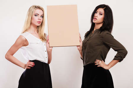 Advertisement concept. Two women caucasian and african holding blank board empty banner cardboard studio shotの写真素材