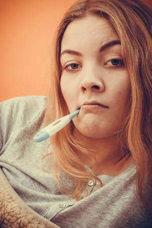 sick ill woman with digital thermometer in mouth. young girl having high fever measuring...