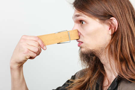 Unpleasant bad smell concept. Portrait of young long haired man with clogged nose by big clothespin.