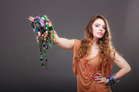 Pretty young woman wearing bracelets and rings holding many plentiful of precious jewelry necklaces beads. Portrait of gorgeous fashion girl in studio on gray.の写真素材