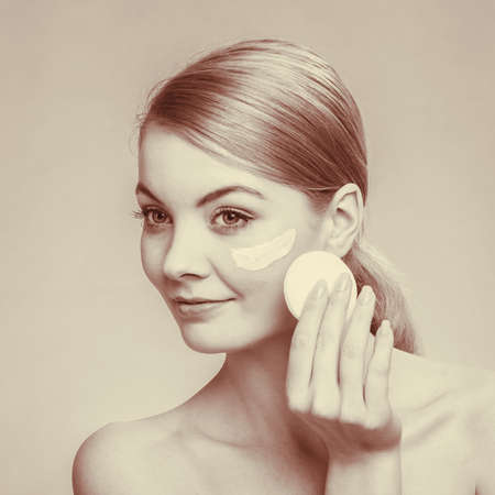 Woman removing makeup with cotton swab pad from face. Young girl taking care of skin. Skincare concept. Sepia toneの写真素材