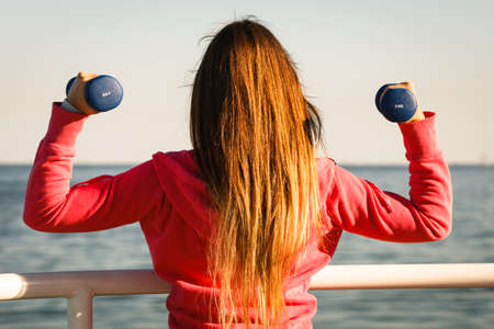 Woman doing sports outdoors with dumbbells. Fit fitness girl in sportswear on seaside exercisingの写真素材