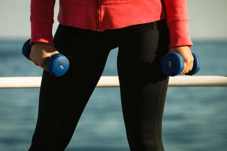 Woman doing sports outdoors with dumbbells. Fit fitness girl in sportswear on seaside exercisingの写真素材