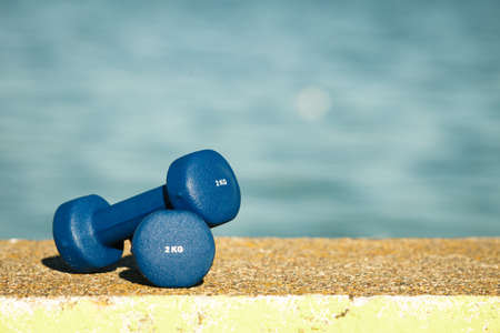 Blue dumbbells sport symbol outdoor on sea shore. Active lifestyle bodybuilding.の写真素材