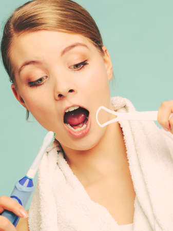 Pretty young girl using electric brush and tongue cleaner with open mouth. Happy woman cleaning her oral cavity caring about dental health.の写真素材