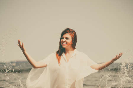 Vacation. Girl splashing water on the coast. Young woman having fun relaxing on the sea. Summertime.