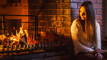Melancholic pensive woman relaxing resting at fireplace. Thoughtful nostalgic young girl heating warming up. Winter at home.の写真素材