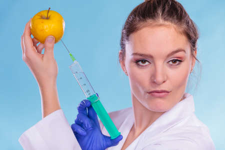 Scientist doctor injecting apple with syringe. Woman chemist holding genetically modified fruit. GM food modification.の写真素材