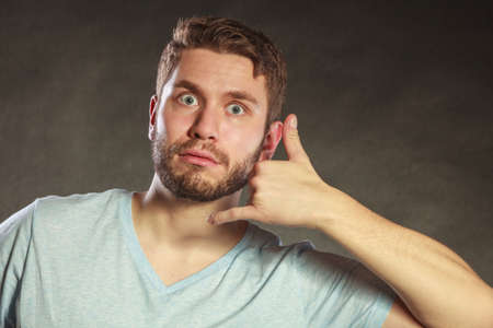 Surprised amazed young man guy with hand palm to ear showing call me gesture in studio on black.の写真素材