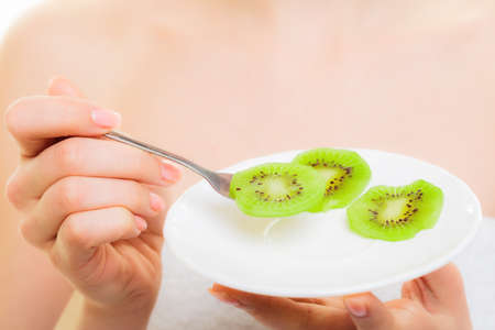 Closeup of plate in female hands. Girl woman eating slices of kiwi tropical fruit isolated on white. Healthy diet and nutrition. Studio shot.の写真素材