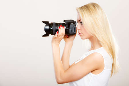Photographer girl shooting images. Attractive blonde woman taking photos with camera, on gray...