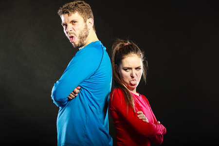 Offended young couple standing back to back after argument quarrel. Woman sticking out tongue....