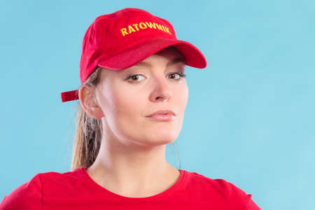 Portrait of lifeguard woman girl in red cap with ratownik sign on blue. Accident prevention rescue.の写真素材