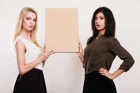 Advertisement concept. Two women caucasian and african holding blank board empty banner cardboard studio shotの写真素材