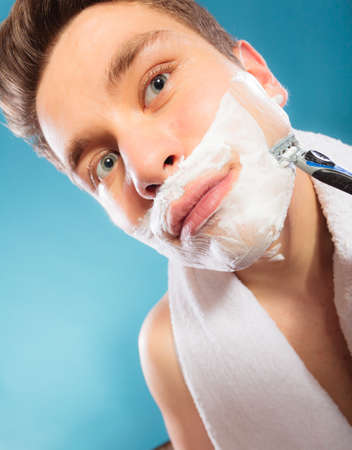 Young man shaving using razor with cream foam. Handsome guy removing face beard hair. Skin care and hygiene.の写真素材