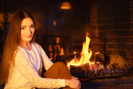 Woman relaxing resting at fireplace. Young girl heating warming up. Winter at home.の写真素材