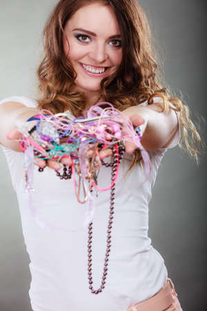 Happy pretty young woman wearing bracelets and rings holding many plentiful of precious jewelry necklaces beads. Portrait of gorgeous fashion girl in studio on gray.の写真素材