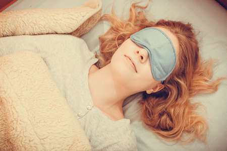 Tired woman sleeping in bed wearing blindfold sleep mask. Young girl taking nap.の写真素材