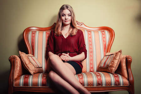 Attractive pretty young woman sitting on vintage retro sofa couch. Elegant fashionable gorgeous girl...