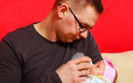 Parenting concept. Happy young father feeding newborn baby girl with milk bottle on couch at home