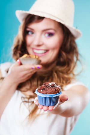 Bakery, sweet food and people concept. Closeup smiling summer woman curly hair straw hat holding cakes cupcakes in hands blue backgroundの写真素材